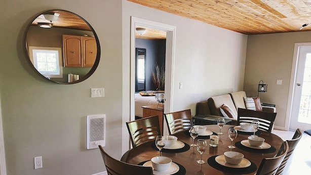 A dining area with a round table set for four, surrounded by wooden chairs. A large mirror hangs on the wall, reflecting the room. - The Cabin on Grey Owl w/hot tub (Onanole)