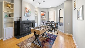 A modern living room with a foosball table, a fireplace, and a dining area with chairs and a table.