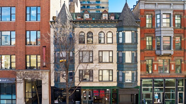 A row of multi-story buildings with various architectural styles, including a corner building with a green awning and a sign for a nail salon.