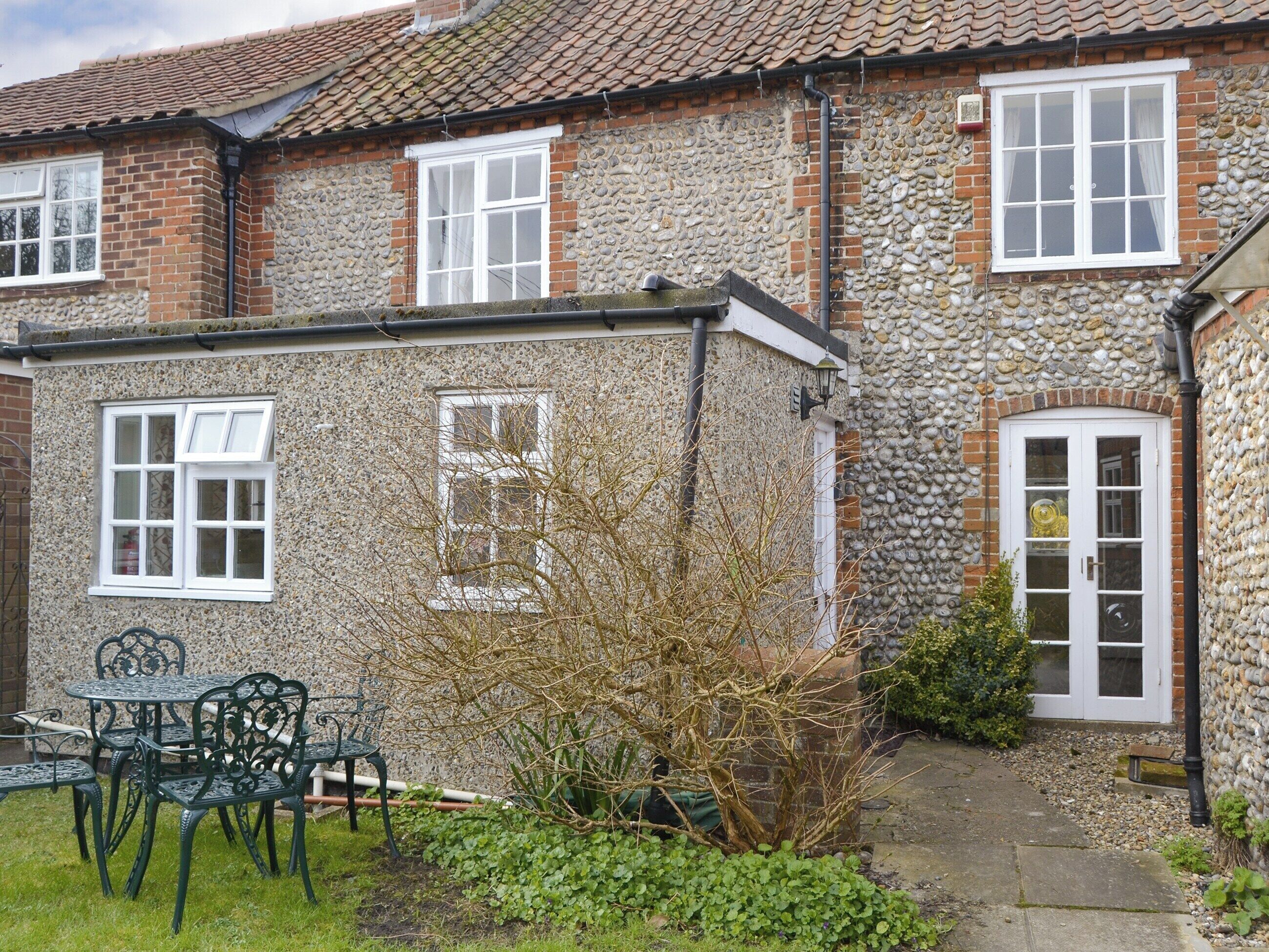 A stone house with a tiled roof, a garden with a table and chairs, and a door with a glass panel.