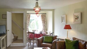 Un salon chaleureux avec un canapé en cuir marron, une table à pois rouges et blancs, et un lustre.