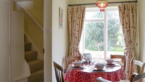 Un coin repas avec une table dressée pour quatre personnes, un escalier et une fenêtre avec des rideaux.