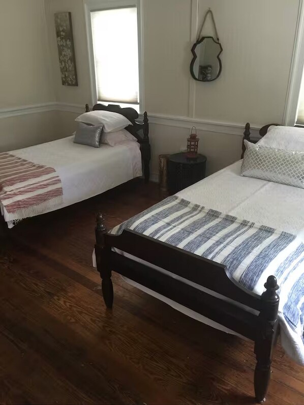 A bedroom with two single beds, wooden flooring, a small table, and a mirror on the wall.