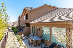 A residential property with a patio area featuring a table and chairs, a large window with blinds, and a satellite dish on the roof.