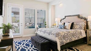 Quarto com cama grande, ventoinha no teto, televisão, escrivaninha e janela com persianas.