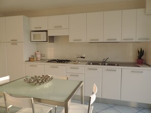 Une cuisine moderne avec des meubles blancs, une cuisinière à gaz, un évier et une table à manger avec des chaises.
