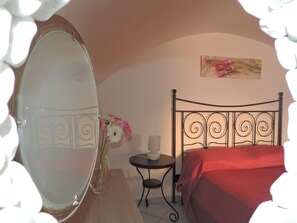Un dormitorio con una cama, una mesita de noche con lámpara, un espejo y un cuadro en la pared.