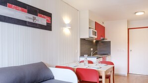 En kompakt opholdsstue med spiseplads, tekøkken og sofa.