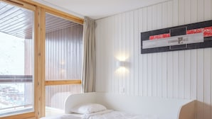 Et soveværelse med seng, et vindue med gardiner og en lampe monteret på væggen.