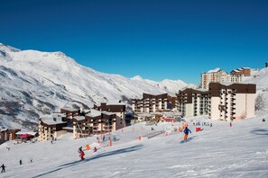 Ein Skigebiet mit mehreren Gebäuden, darunter Hotels und Restaurants, sowie eine Skipiste mit Skifahrern.