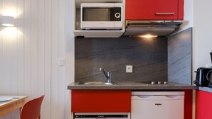 Een kleine keuken met een magnetron, vaatwasser en een rode kast.
