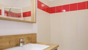 Een badkamer met een houten wastafelmeubel, een witte wastafel, een spiegel en een douchegedeelte met rode tegels.
