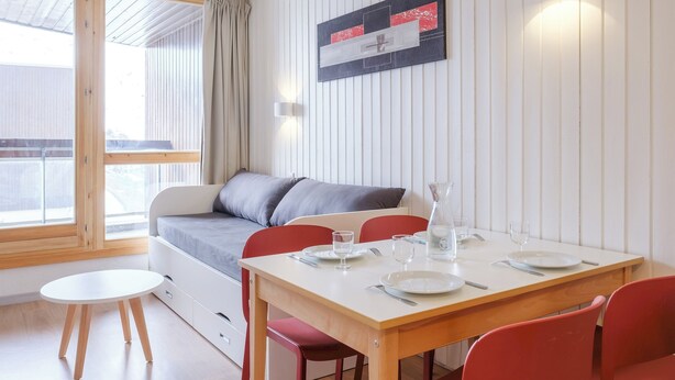 Et moderne værelse med et træspisebord, røde stole, en grå sofa og en hvid væg med et indramet kunstværk.