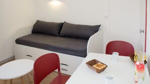 A compact room with a sofa bed, a dining table, two chairs, and a small breakfast setup. - travelski home select - Résidence Les Lys - Studio 2 personnes Bâtiment B (Les Menuires)