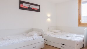 Een kamer met twee witte bedden, een wandlamp en een raam met houten kader.