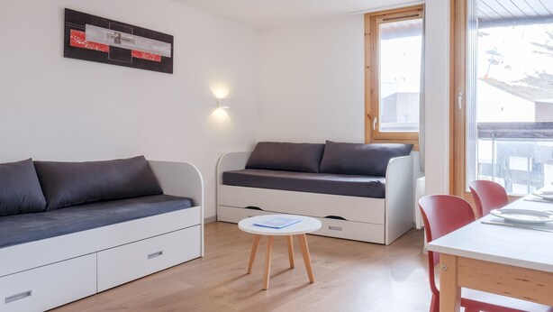 Een moderne, compacte leefruimte met een bank, een klein tafeltje en een eethoek met stoelen.