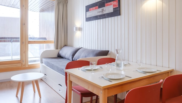 Ein modernes Zimmer mit einem Holztisch, roten Stühlen, einem weißen Sofa und einem großen Fenster.