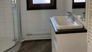 Un baño con cabina de ducha de vidrio, ventana con cristal satinado y lavabo con espejo.