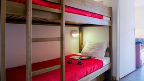 Una cama individual con ropa de cama roja, una lámpara de noche y una mesita de noche pequeña con un libro y un control remoto.
