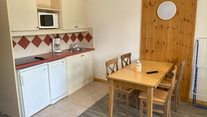 Cocina compacta con microondas, cafetera y pileta. Se observa una mesa de madera con sillas y un refrigerador pequeño.