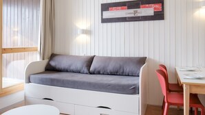 Une pièce avec un canapé blanc, une table à manger avec des chaises rouges et un luminaire fixé au mur.