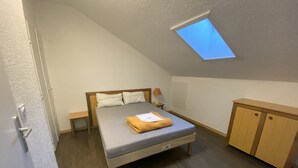 Ein Schlafzimmer mit Oberlicht, einem Bett mit Kissen, einem Nachttisch, einer Lampe und einem Holzschrank.