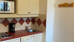 Eine kleine Küche mit weißen Schränken, einer Mikrowelle, einer Kaffeemaschine, einem Geschirrspüler und einem Mülleimer.