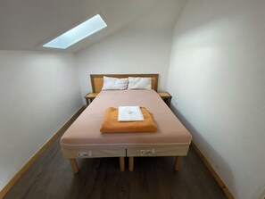 Ein kleines, aufgeräumtes Schlafzimmer mit einem Einzelbett, zwei Nachttischen und einem Oberlicht.