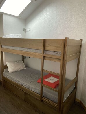 Un letto a castello con una finestra a lucernario sopra, una parete bianca e un pavimento in legno.