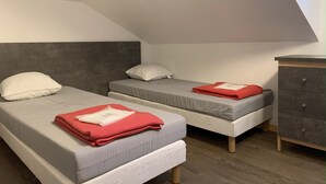 Ein kleines, modernes Schlafzimmer mit zwei Einzelbetten, einer grauen Kopfstütze und einer Holzkommode.