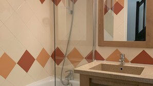 Ein Badezimmer mit Duschkabine, Waschbecken mit Spiegel darüber und Fliesenwand mit Rautenmuster.