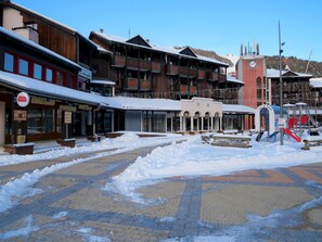 A snow-covered plaza with buildings, including a restaurant and a hotel. - travelski home classic - Résidence La Muzelle - 2 pièces 4/5 personnes Bâtiment B (Les Deux Alpes)