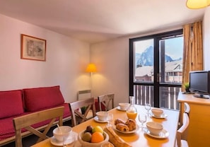 Un coin repas avec une table mise pour le petit-déjeuner, comprenant des croissants, des fruits et un verre de jus d’orange.