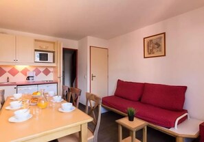 Un espace de vie compact comprenant un coin cuisine, une table à manger pour deux personnes et un canapé rouge.