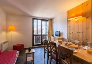 Une chambre d’hôtel compacte comprenant un lit, une petite table, un coin repas, un téléviseur et une grande fenêtre donnant sur un beau paysage.