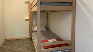 Uma cama beliche com estrutura de madeira, colchão, travesseiros e um cobertor vermelho.