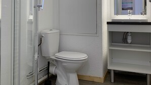 Un baño con cabina de ducha de vidrio, inodoro blanco y lavamanos con espejo.