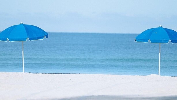 Two blue beach umbrellas on a sandy beach with a calm sea in the background.