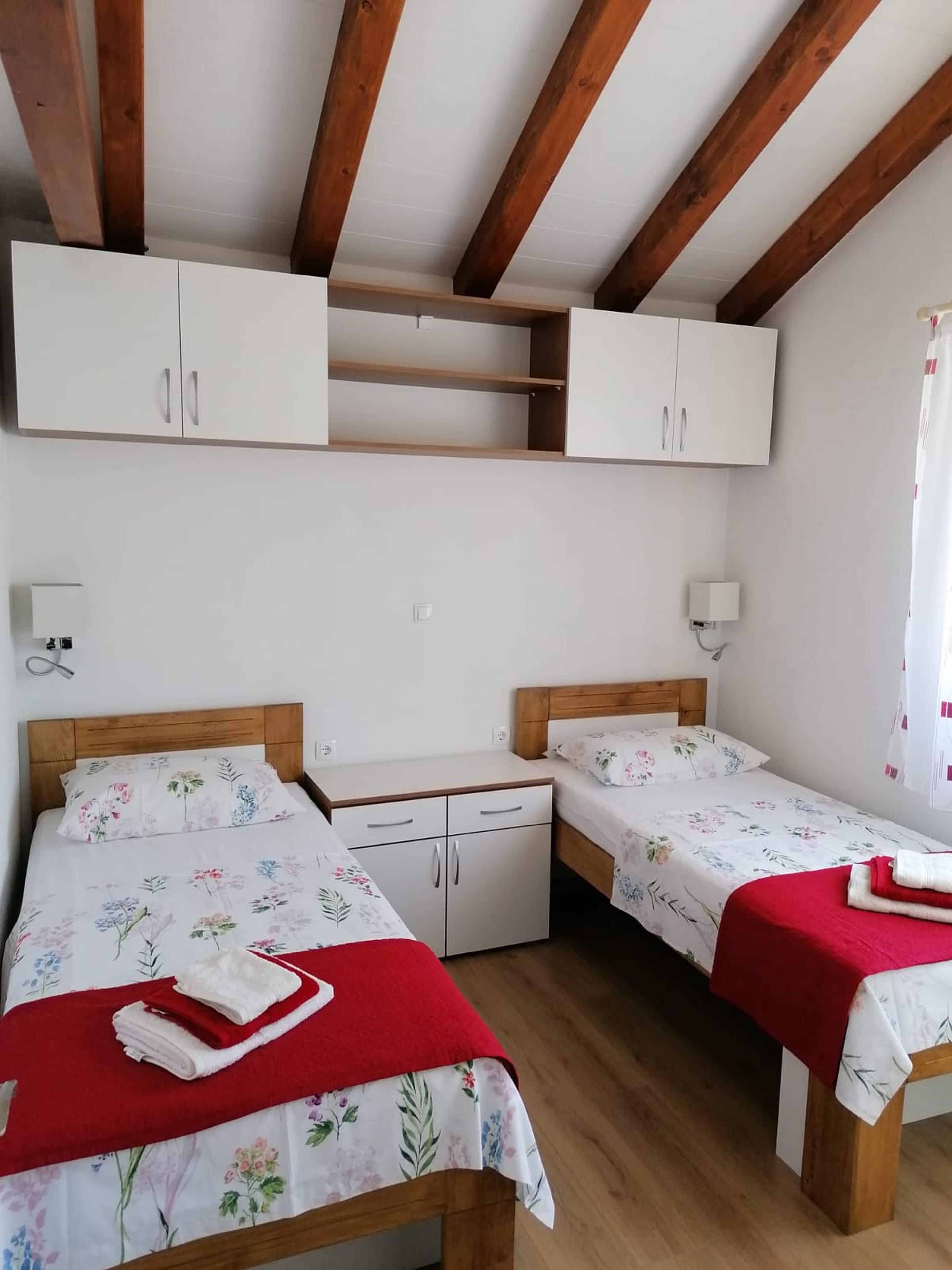 A bedroom with two beds, wooden headboards, white cabinets, and a wooden ceiling.