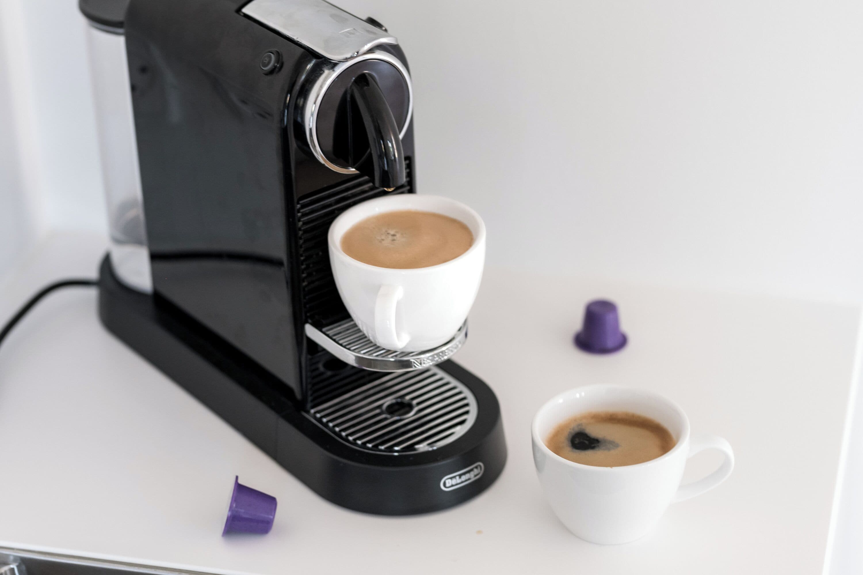 Una máquina de café espresso negra con una taza blanca de café delante.