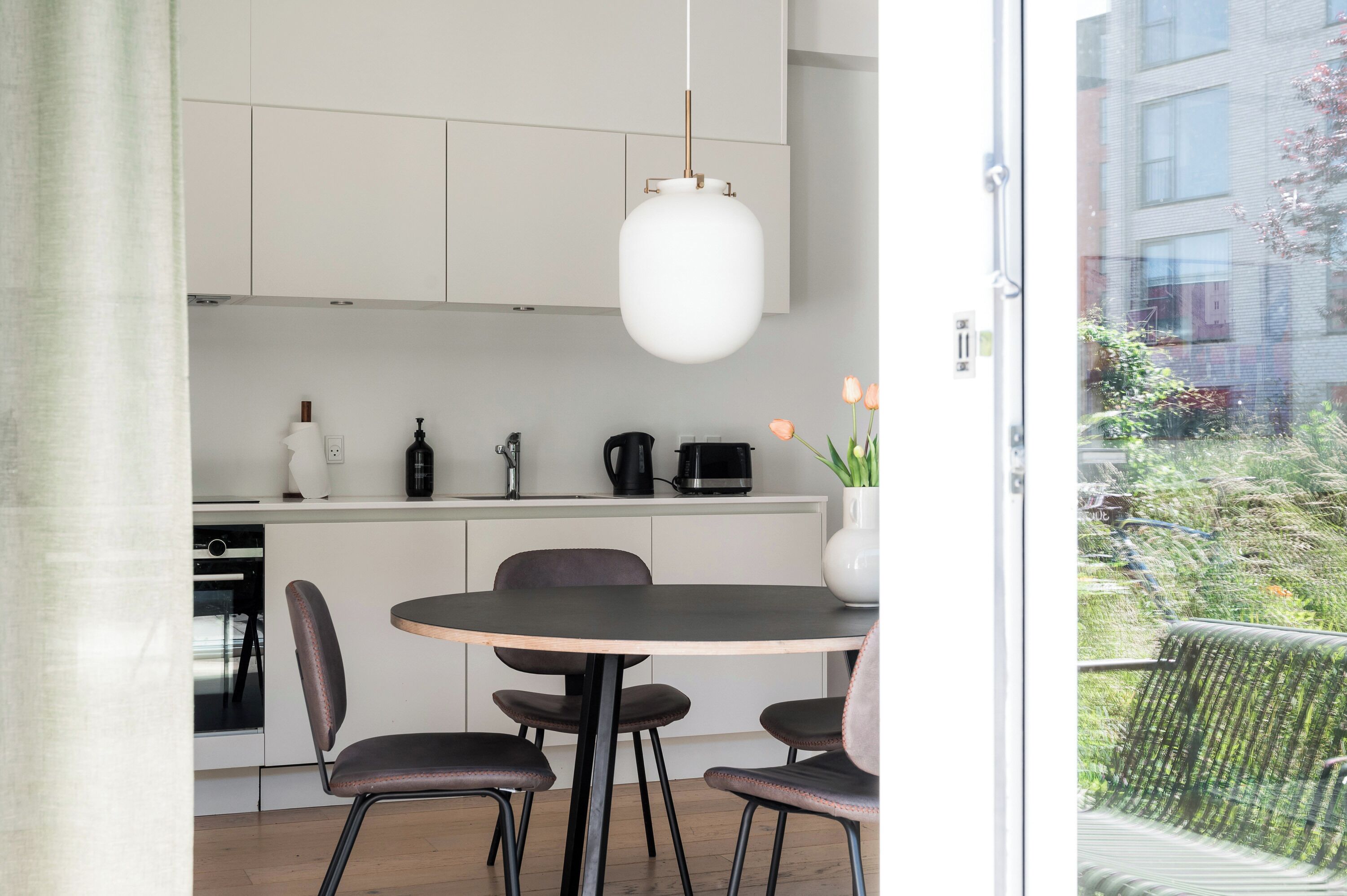 Een moderne keuken met witte kastjes, een ronde eettafel en een hanglamp.
