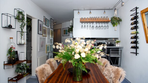 Ein moderner Essbereich mit einem Holztisch, einer Blumenvase und einer Küche im Hintergrund.