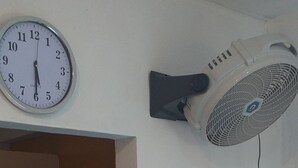 Een kamer met een bed, een wandventilator, een klok en een stopcontact.