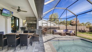 A backyard with a pool, outdoor furniture, and a TV mounted on the wall. - Amazing Outdoor kitchen & Private Screened In Pool (Bonita Springs)