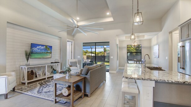 A spacious living area with a large sofa, a coffee table, and a TV mounted on the wall. There is a kitchen area with a countertop and a refrigerator. - Amazing Outdoor kitchen & Private Screened In Pool (Bonita Springs)