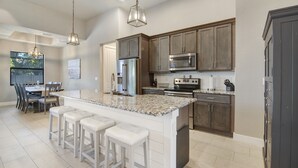 A spacious kitchen with granite countertops, stainless steel appliances, and a large island with bar stools. - Amazing Outdoor kitchen & Private Screened In Pool (Bonita Springs)