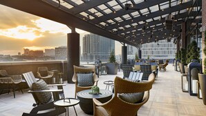 Una terraza en la azotea con mobiliario de mimbre, techo de cristal y vistas a la ciudad al atardecer.