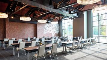 A spacious indoor dining area with multiple tables and chairs, large windows, and a brick wall.