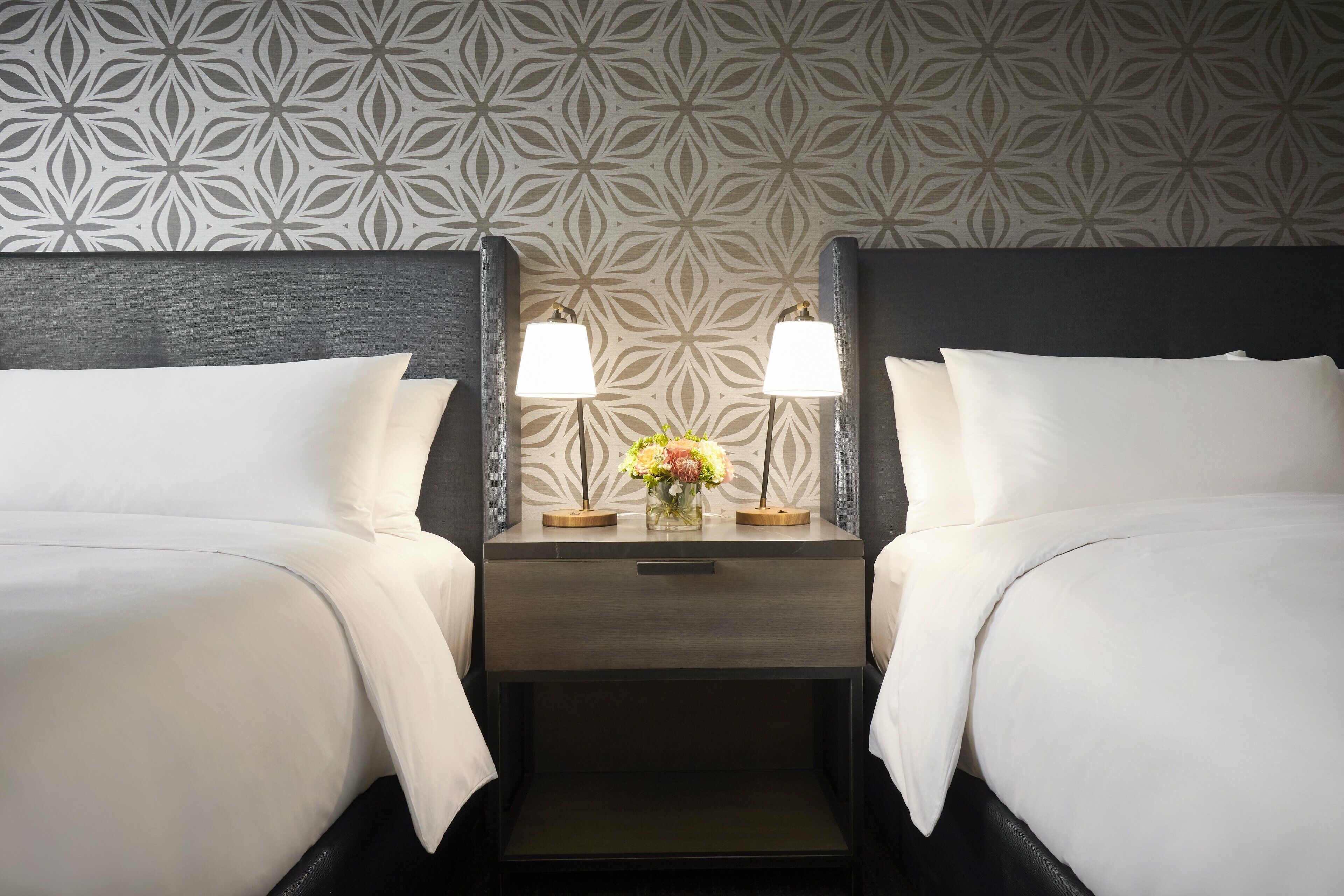 Habitació d'hotel amb dos llits, calaixos amb làmpades i un ram de flors.