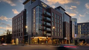 Un hotel de varios pisos con un llamativo letrero que dice "ARCHER HOTEL", un bar en la planta baja y una fachada moderna de vidrio.